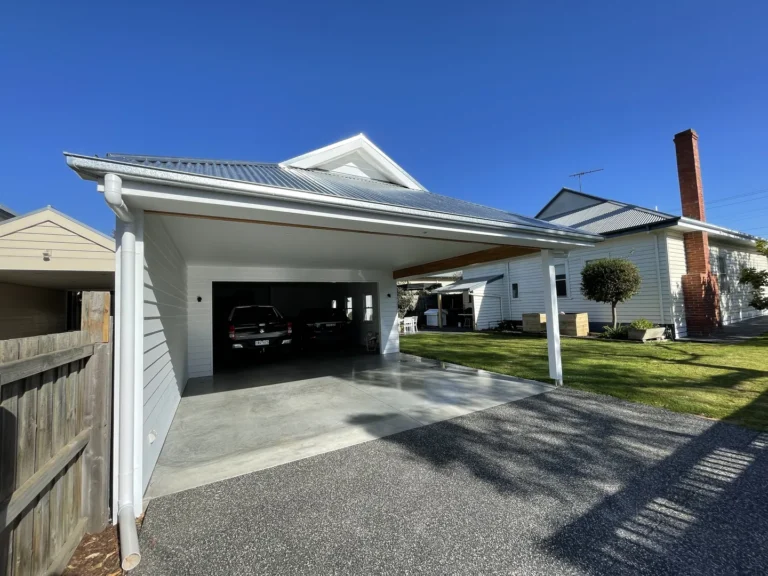 Carport with solar panels beside white house on sunny day.